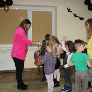Pani Dyrektor Paulina Frontczak-Pawłowska częstuje dzieci upominkami z kosza wiklinowego.