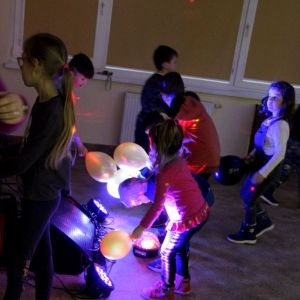Grupka dzieci tańcząca z balonikami przy migających kolorowych światełkach.
