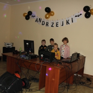 Czterej chłopcy na tle dekoracji z napisem „Andrzejki", stoją przy sprzęcie didżeja.