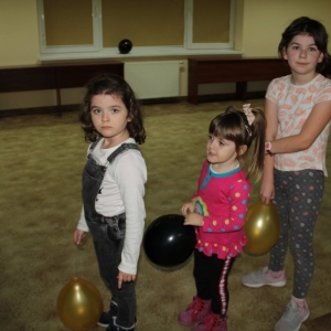Trzy dziewczynki z balonikami stoją cierpliwie w kolejce.