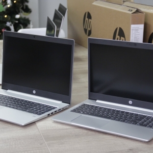 Otwarte laptopy HP ustawione na stole a za nimi opakowania po nich.