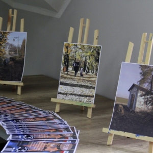 Komplet wypełnionych dyplomów zwycięzców konkursu rozłożone na stole wraz z wydrukowanymi zdjęciami leżącymi na podpórkach.  