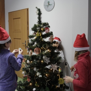 Dzieci w czapkach Mikołaja dekoruję choinkę.