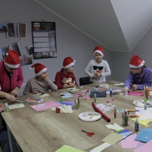 Dzieci z czapkami Mikołaja siedzą przy stole i robią kartki świąteczne.