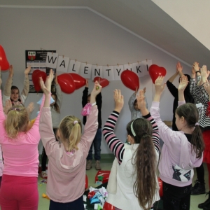 Dzieci stoją w kółku i podnoszą ręce do góry w których mają baloniki w kształcie serca.