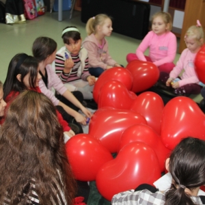 Dzieci siedzą wokół balonów w kształcie serca.