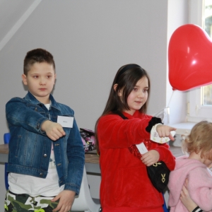 Chłopiec i dziewczynka z balonikiem w kształcie serca wskazują na coś palcem.