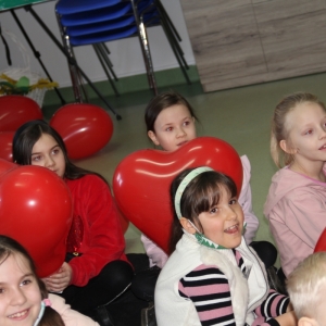 Skupione dzieci siedzą z balonikami w kształcie serca.