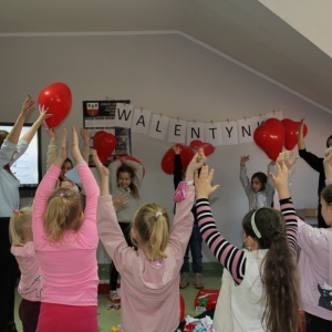 Dzieci stoją w kółku i podnoszą ręce do góry w których mają baloniki w kształcie serca.