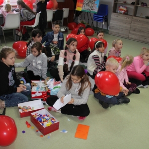 Skupione dzieci siedzą z balonami w kształcie serca i robią walewntynki.