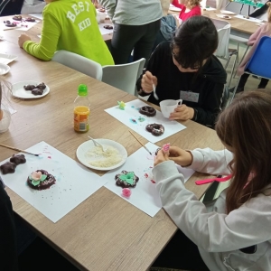 Dzieci dekorują pierniczki przy stołach.
