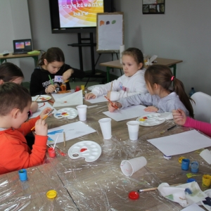 Dzieci siedzą przy stołach i malują.