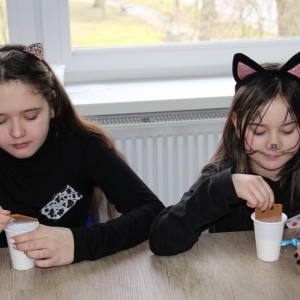 Dziewczynki przebrane za czarne koty jedzą przekąskę.