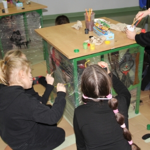 Dzieci dekorują stoliki malując na nich koty.