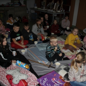 Dzieci z zainteresowaniem oglądają film wyświetlany przez projektor zajadając w tym czasie przekąski.