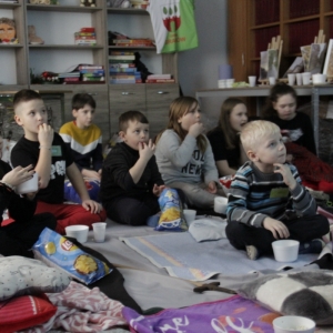 Dzieci z zainteresowaniem oglądają film wyświetlany przez projektor zajadając w tym czasie przekąski.