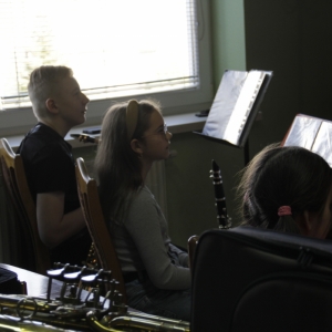 Dzieci siedzą z instrumentami muzycznymi i są skupione na nauczycielu.