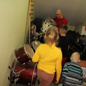 Nauczyciel wraz z dziećmi wyciąga instrumenty muzyczne ze schowka.