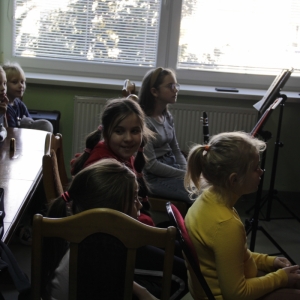 Dzieci siedzą i uważnie słuchają nauczyciela.