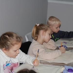 Dzieci siedzą przy stole i malują piękne ozdoby na torbach.