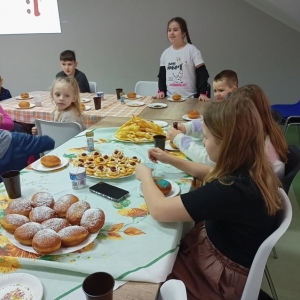 Dzieci siedzą przy stole zastawionym pączkami i ciastkami.