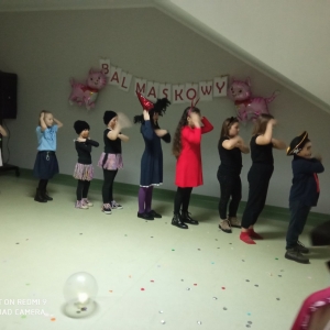Dzieci w różnych kostiumach tańczą razem w rzędzie.