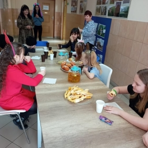 Dzieci siedzą przy stołach i zajadają słodkie przekąski popijając je herbatą.