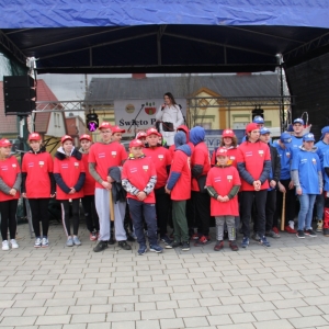 Zdjęcie grupowe drużyny w czerwonych i niebieskich strojach do gry w Palanta na tle sceny, na której stoi Pani Dyrektor GCKB Grabów. 