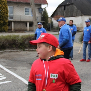 Chłopiec z czerwonej drużyny na tle innych uczestników gry w Palanta z drużyny niebieskich.