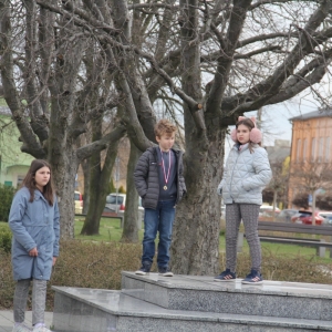 Dwie dziewczynki i chłopiec z medalem na szyi stoją na tle drzewa.