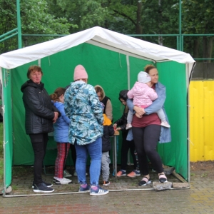 Grupka dzieci wraz z rodzicami przy zielonym stoisku dla dzieci na pikniku „Dzień Rodziny" w Grabowie.