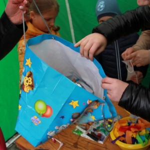 Grupka dzieci przy zielonym stoisku częstuje się smakołykami z niebieskiej torby.