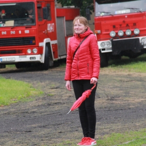 Uśmiechnięta pani w czerwonej kurtce na tle dwóch wozów strażackich.