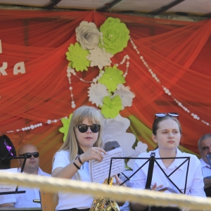 Grupka dziewczynek i innych osób z Orkiestry Dętej w Grabowie siedzą ze skupieniem na scenie trzymając każdy z nich po instrumencie muzycznym. 