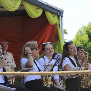 Grupka dziewczynek z Orkiestry Dętej w Grabowie siedzą uśmiechnięte na scenie trzymając każda z nich po instrumencie muzycznym. 