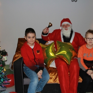 Mężczyzna przebrany za Świętego Mikołaja i chłopcy pozują do zdjęcia na kanapie.