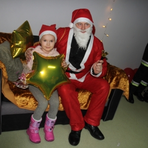 Mężczyzna przebrany za Świętego Mikołaja i dziewczynka z balonem w kształcie gwiazdy pozują do zdjęcia na kanapie.