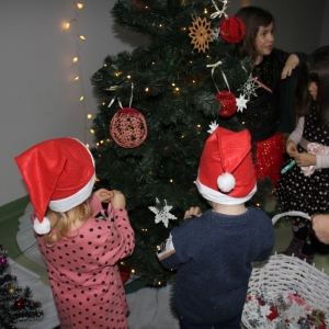 Dwójka małych dzieci w czapkach Mikołaja ozdabia choinkę.