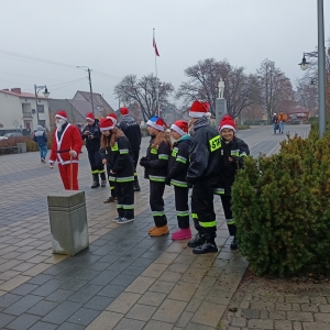 Dzieci przebrane za straż pożarna w czapkach Mikołaja stoję w rzędzie.