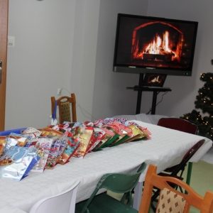 Zapakowane prezenty świąteczne ułożone na stole a w tle telewizor z ogniskiem.
