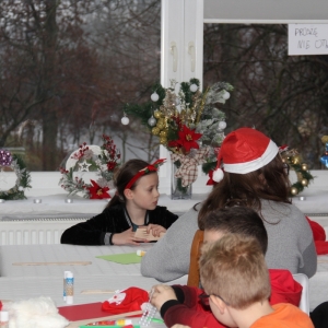 Dzieci siedzą przy stołach i robią ozdoby świąteczne.