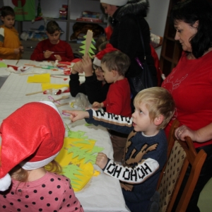 Chłopiec przy stole pełnym dzieci robiących ozdoby świąteczne wskazuje na coś palcem.