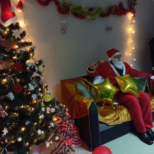 Mężczyzna przebrany za Świętego Mikołaja pozuje na kanapie z dzwonkiem i balonami w kształcie gwiazd.