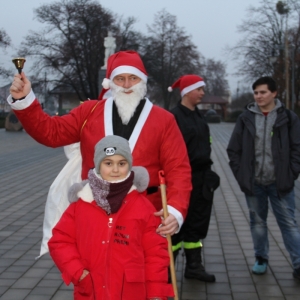 Mężczyzna przebrany za Świętego Mikołaja pozuje do zdjęcia z chłopcem i dzwonkiem w ręku.