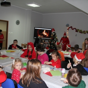 Dzieci siedzą przy stołach i robią ozdoby świąteczne.