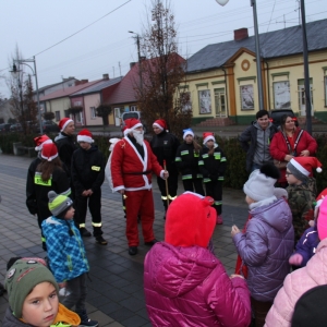 Grupa dzieci, straży pożarnej, dzieci przebranych za straż pożarną i mężczyzna przebrany za Świętego Mikołaja.