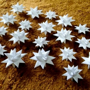 Wyeksponowanych na złotym tle kilkanaście białych gwiazdek zrobionych z białej tasiemki.