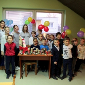 Zdjęcie grupowe dzieci wraz z Panią Dyrektor Pauliną Frontczak-Pawłowską i panią prowadzącą, którzy stoją wokół stołu zastawionego stroikami świątecznymi.