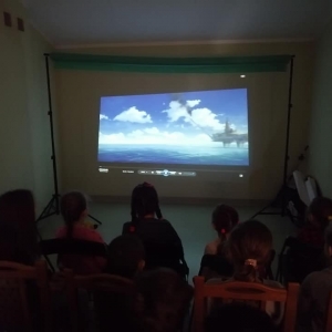 Dzieci oglądają film wyświetlany na projektorze. 