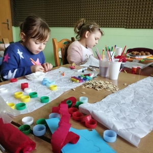 Dzieci bawią się przy stole zastawionym przyborami plastycznymi.